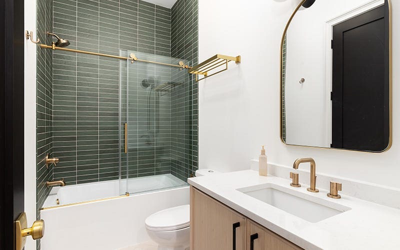 Une salle de bain contemporaine avec des carreaux verts vibrants et des luminaires en or chic, mettant en valeur un mélange de couleur et d'élégance