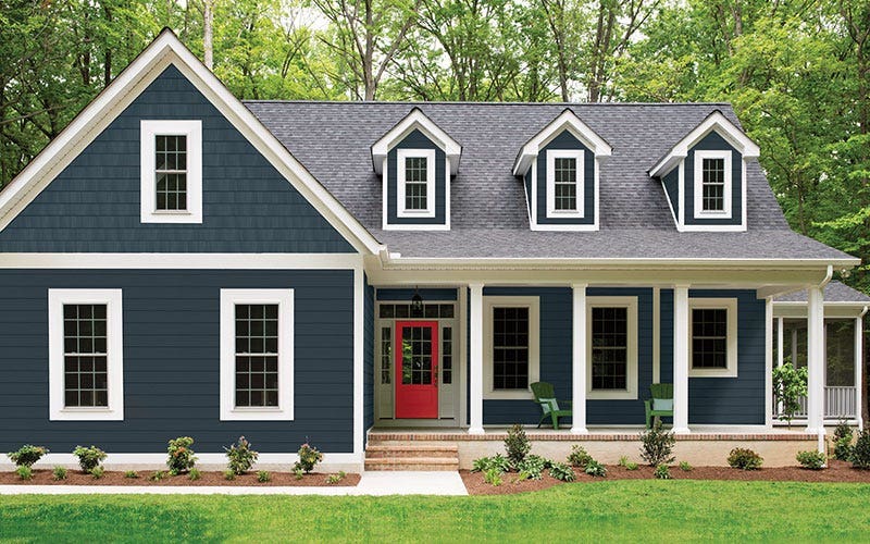 A blue house featuring white trim and a bright red door, set against a clear sky.