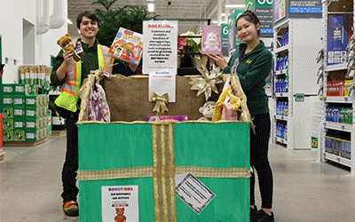 Two store associates assist customers with a box of toys, highlighting community support and gift-giving in a vibrant store setting