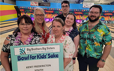 Community members gather, displaying a sign for a bowling fundraiser aimed at supporting children in need